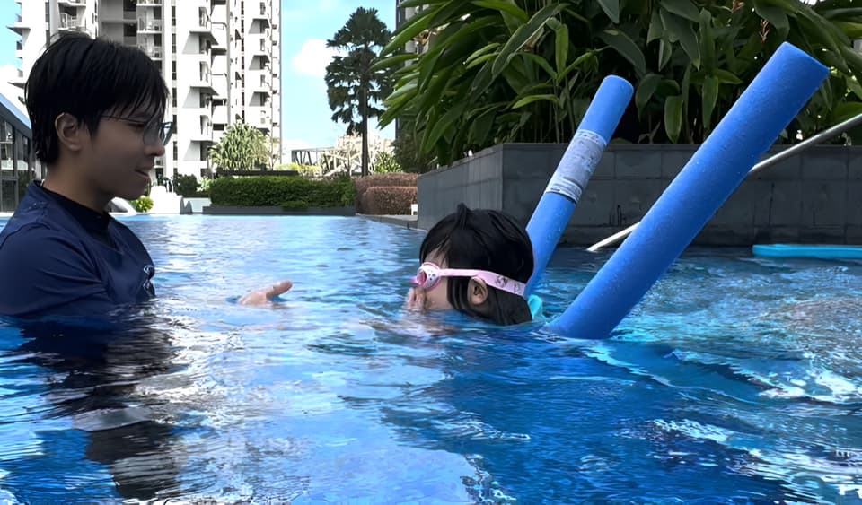 A Poolva coach guiding a young girl in pink goggles as she practises floating in a condo pool