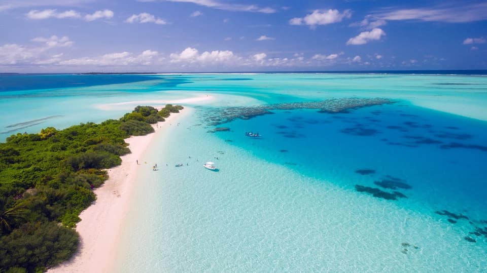 Aerial view of a white sand island surrounded by clear turquoise water