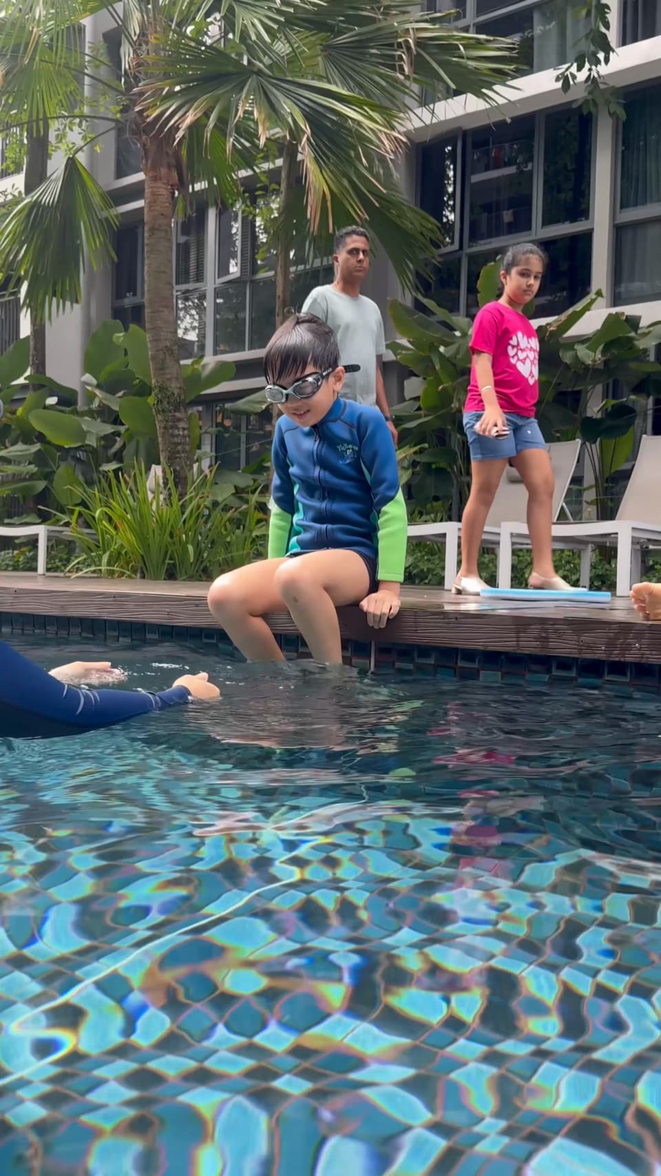 A young child sitting at the edge of a condo pool while parents watch